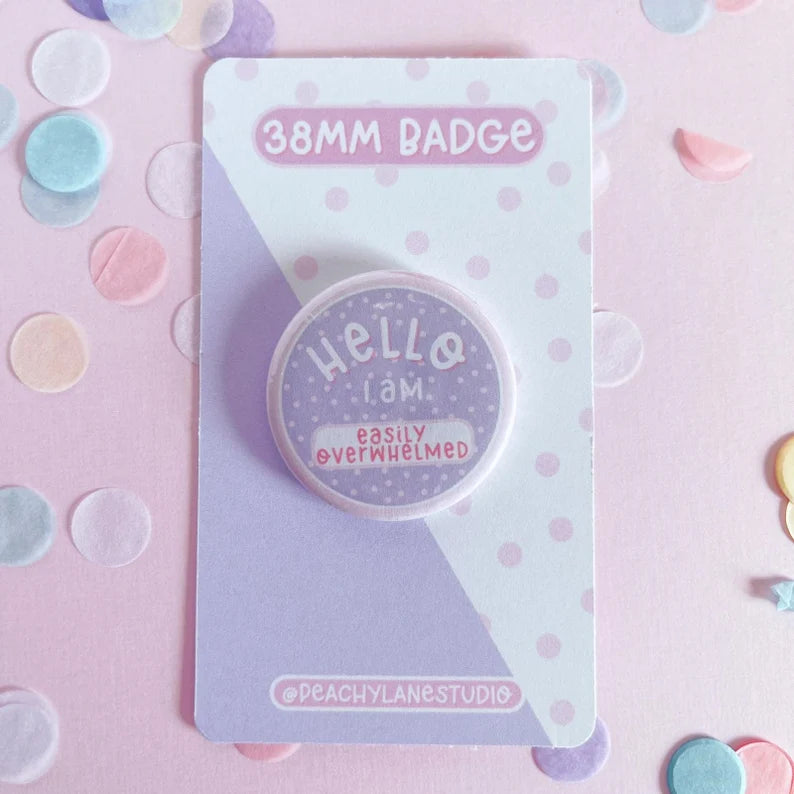 Badge with 'Hello, I am easily overwhelmed' text on a polka dot card with '38MM BADGE' text.