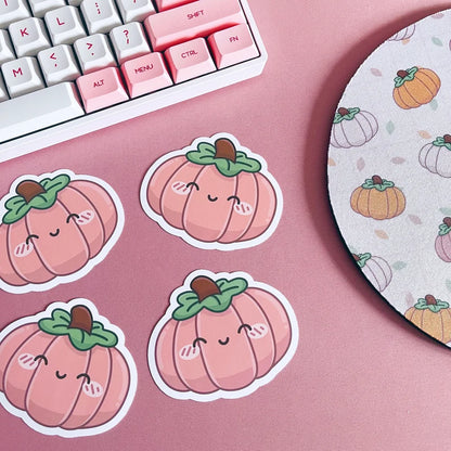 Cute pumpkin stickers on a pink surface with a keyboard and mouse pad in the background.